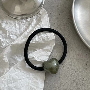 Close-up of a black elastic hair tie with a polished dark green heart charm on white paper