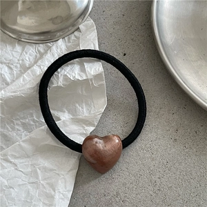 Detail of a black elastic hair tie with a brown metallic heart charm on a gray surface