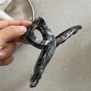 Dettaglio della molletta per capelli incrociata con texture in marmo bianco e nero