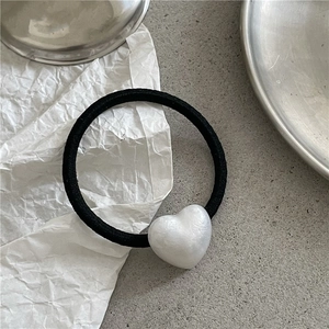 Minimalist black elastic hair tie with a textured white heart charm on a gray background