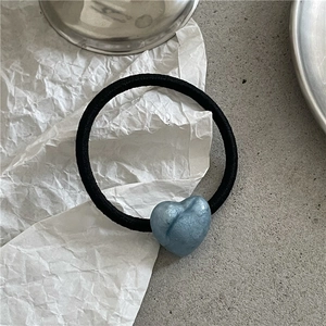 Detail shot of a black elastic hair tie featuring a pearlescent blue heart charm on paper