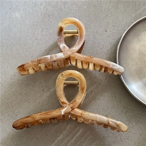 Dettaglio di grandi mollette per capelli effetto marmo con molla dorata e design incrociato