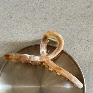 Dettaglio di un grande fermaglio per capelli marmorizzato con molla in metallo dorato