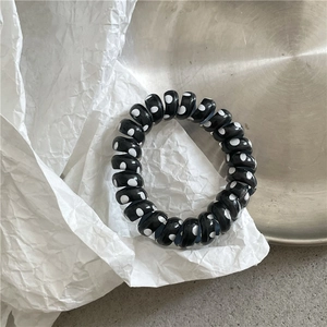 Detail shot of black spiral hair tie with white polka dots on a textured metallic surface