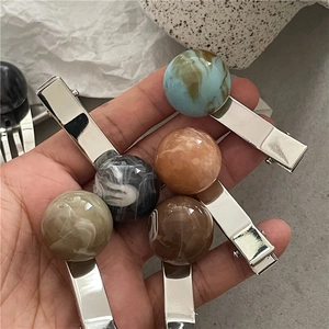 Close-up of marble pattern resin beads on silver metal hair clips held in hand