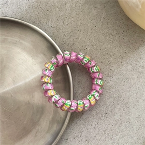 Close-up of pink telephone wire hair tie with colorful graffiti spots on a silver tray