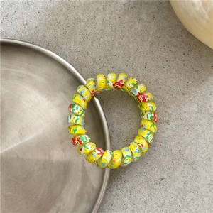 Macro shot of yellow spiral hair tie with colorful graffiti patterns on metal tray