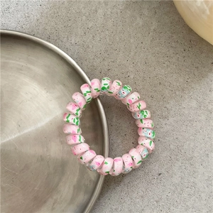 Detailed view of a pink spiral hair tie with colorful graffiti patterns on metal tray