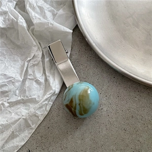 Close-up of silver metal hair clip with blue and brown marble textured sphere ornament