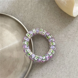 Close-up of elastic spiral hair tie with purple floral graffiti pattern on grey surface
