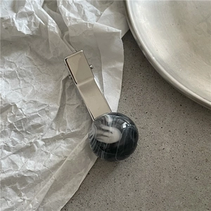 Detail shot of a silver hair clip featuring a black and white marble sphere on textured paper