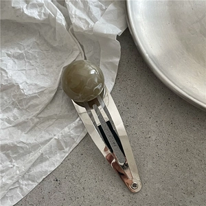 Detail of silver metal hair clip featuring a large olive green marble patterned bead charm