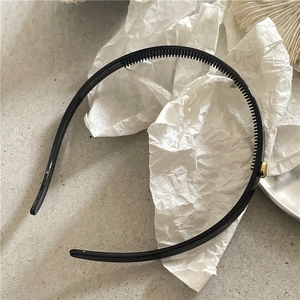 Detail of black non-slip headband with fine inner teeth and round gold metal accent