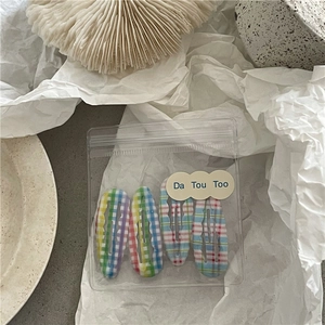 Détail de 4 barrettes BB à carreaux en tissu dans une pochette de rangement en PVC