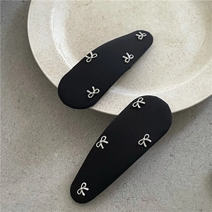 Détail de pinces à cheveux en tissu noir avec des petits nœuds en métal argenté