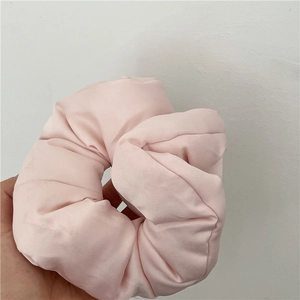 Dettaglio di un elastico per capelli in raso rosa chiaro tenuto in mano su muro bianco