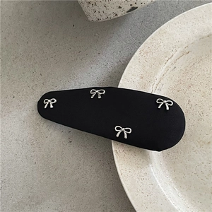 Détail de la barrette en tissu noir avec des nœuds argentés sur une surface céramique