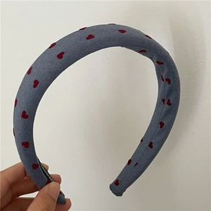 Detail of grey padded headband with red heart prints and a black handmade woven label