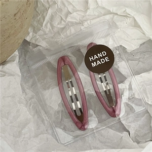 Detail of purple marble hollow oval hair clips in handmade packaging on white textured paper