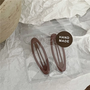 Detail of two brown oval hair clips in handmade packaging on aesthetic background