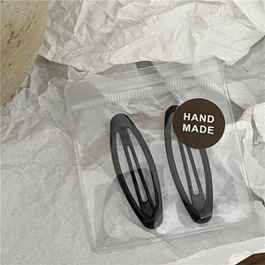 Detail of two black teardrop metal BB hair clips with handmade label in clear packaging
