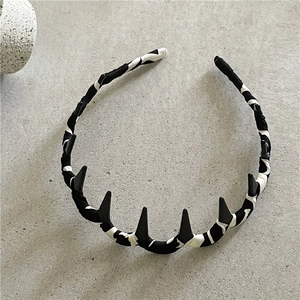 Detail of fabric wrapped headband with matte black decorative spikes on stone background