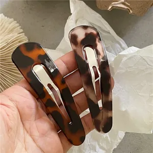Detailed close-up of retro leopard print hair clips held by hand with metal spring clips