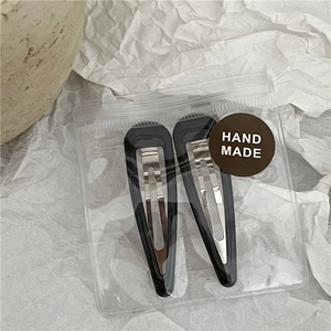 Close-up of black teardrop snap hair clips in transparent bag with hand made sticker