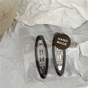 Detail view of two black oval BB hair clips with HAND MADE sticker in a poly bag