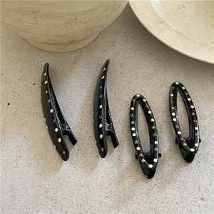 Close-up of four black hair clips with colorful polka dots in oval and curved shapes