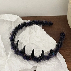 Detail of purple plush headband with black punk spikes on wood and white paper
