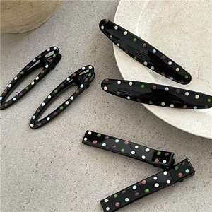 Fashionable black hair clips with colorful polka dots in various shapes on a stone background