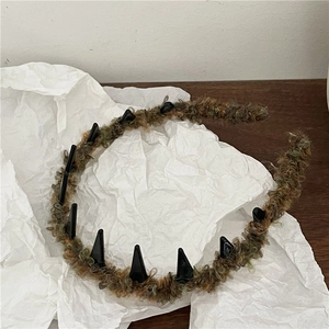 Detail of brown and green fuzzy headband with unique black triangular punk spikes decor