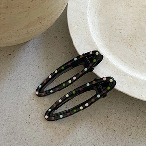 Detail of two black polka dot duckbill hair clips on white ceramic plate background