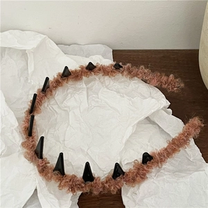Close-up of pink fuzzy headband with black decorative spikes on a textured background