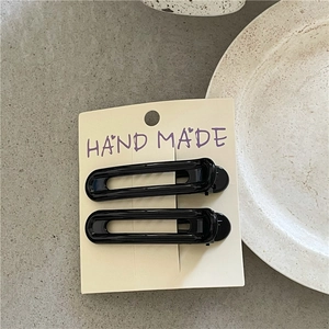 Close-up of two black hollow geometric hair clips on a white handmade display card