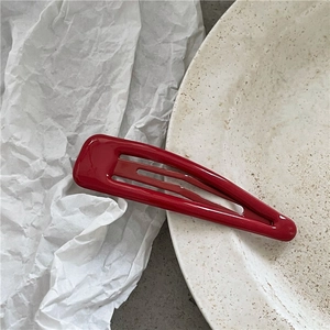 Dettaglio di un fermaglio per capelli rosso lucido a forma di goccia su fondo bianco