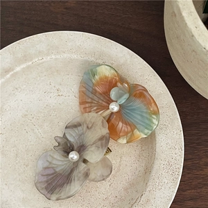 Macro detail of orchid hair clips in marble acetate with central pearl on ceramic plate