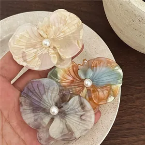 Macro detail of acetate orchid hair clips with pearlescent texture and central white pearls