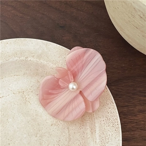 Detail shot of a pink acetate flower hair clip with a pearl center on a ceramic plate
