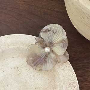 Detailed close-up of an orchid hair clip with pearlescent acetate texture and pearl center