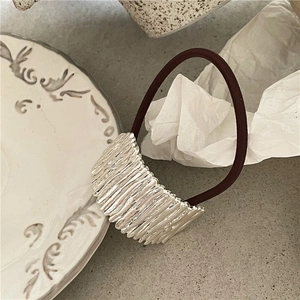 Close-up of wavy metal texture on a hair scrunchie over a vintage ceramic plate