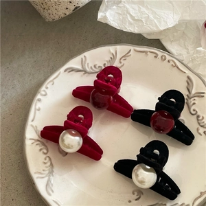 Detail of velvet cross hair claws with pearls and resin beads on a ceramic plate