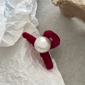 Detail of red velvet bow hair clip with a large white pearl center on a neutral background