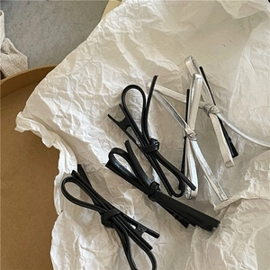 Détail de barrettes à nœuds en similicuir argenté et noir sur fond de papier blanc