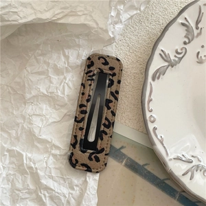 Detailed macro view of a leopard print fabric hair clip on a white textured background