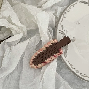 Detail view of a knitted teardrop hair clip with a vintage porcelain plate and paper background