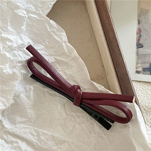 Détail d'une pince à cheveux à nœud en cuir PU bordeaux avec clip en métal noir