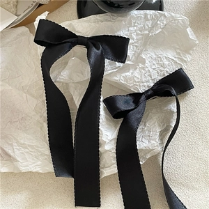 Detail of long black satin ribbon bow hair clips with scalloped edges on paper