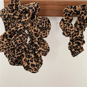 Set of two leopard print hair scrunchies in varied sizes on a wooden display rod